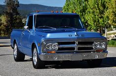 an old blue truck is parked on the side of the road with trees in the background