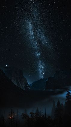 the night sky is filled with stars above mountains and trees in the foggy valley