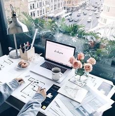 a laptop computer sitting on top of a white table next to a vase filled with flowers