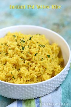 a white bowl filled with yellow rice on top of a blue and green table cloth