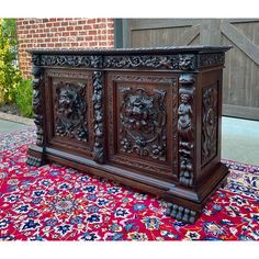 an ornately carved wooden cabinet sitting on top of a colorful rug in front of a brick building