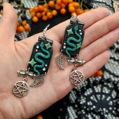 a pair of earrings with green and black designs on them, in the palm of someone's hand