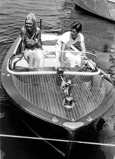 two people sitting on the back of a boat in the water with another person standing next to them