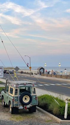 an old jeep is parked on the side of the road by the beach and ocean