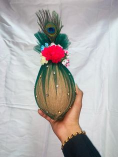 a person holding a vase with flowers and feathers on it's head in front of a white backdrop