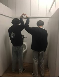 two men standing in front of a urinal with their hands on each other's heads