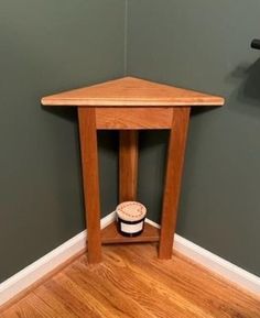 a small wooden table with a cup on it's side in front of a green wall