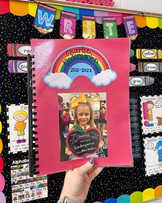 a child's hand holding up a pink book with a rainbow on it