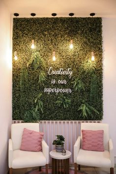 two white chairs in front of a green wall with words on it and lights above them