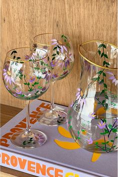 three wine glasses sitting on top of a mat with flowers painted on the glassware