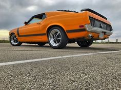 an orange muscle car parked on the side of the road with dark clouds in the background