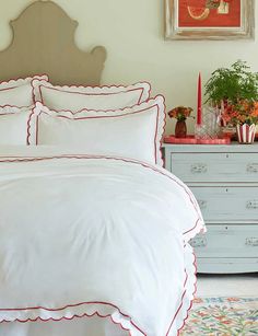 a bed with white sheets and red trimmings in front of a painting on the wall