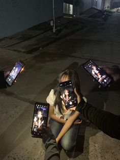 several people holding up cell phones with pictures on them in the middle of an empty street