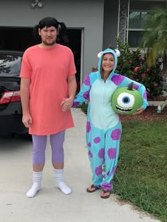 a man and woman dressed in costumes standing next to each other on the driveway with cars parked behind them