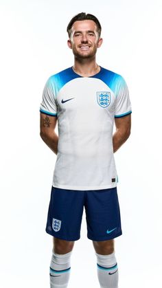 a man is posing for a photo in his england jersey and soccer shorts, wearing nike socks