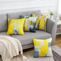 a gray couch with yellow and grey pillows on it in a living room area next to a rug