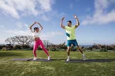 two people are doing yoga outside in the grass with their hands up and arms raised