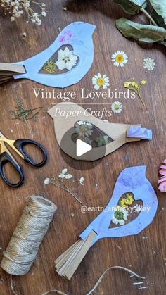 paper flowers and scissors sitting on top of a wooden table next to twine spools