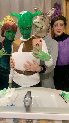 three people dressed in costumes are taking a selfie with their cell phones while standing in front of a bathroom sink