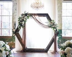 a wedding arch decorated with flowers and greenery in front of a chandelier