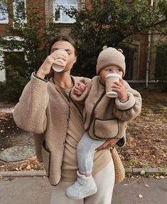 two women drinking coffee while standing in front of a house with their baby on her lap