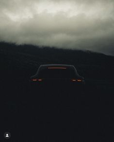 a car parked in the dark on a cloudy day with mountains and clouds behind it