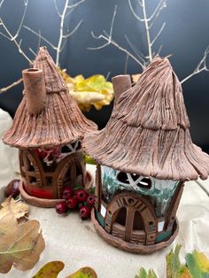 two clay houses sitting on top of a table covered in leaves and berries next to each other