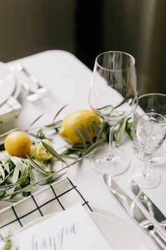 the table is set with white plates and silverware, wine glasses and lemons