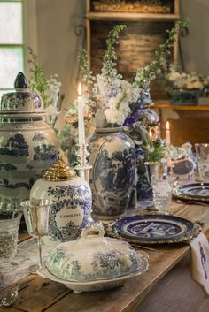 the table is set with blue and white dishes, candles, and flowers in vases