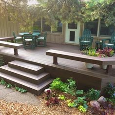 a wooden deck with green chairs and plants on the steps next to it, in front of a house