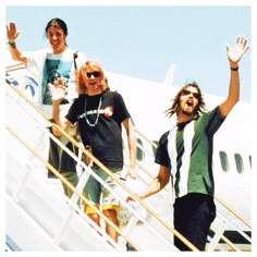 two men and a woman are walking up the stairs to an airplane with their hands in the air