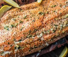 a close up of a fish on a grill with lemon wedges and seasoning