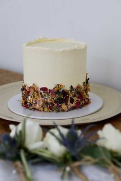 a white frosted cake sitting on top of a table next to flowers and greenery