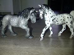 two toy horses standing next to each other on a wooden floor