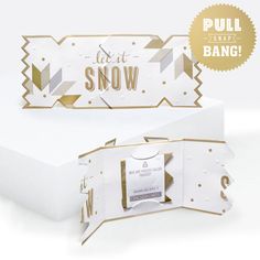 an open white box with gold foil on it and the words, let it snow