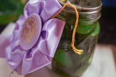 a jar filled with green pickles and a purple bow tied around the top, sitting on a table