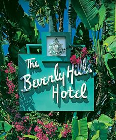 the beverly hills hotel sign is surrounded by palm trees and purple flowers in front of it