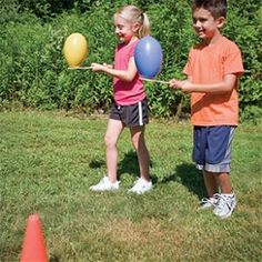 two young children playing with balloons in the grass, one holding a stick and the other looking at it