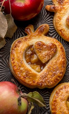 apple pies on a plate with apples and leaves around them in the shape of a heart