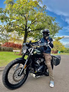 a man sitting on top of a motorcycle in the middle of a road next to a tree