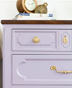 a close up of a purple dresser with books on top and a clock in the background