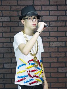 a young man wearing glasses and a hat holding a cell phone to his ear while standing in front of a brick wall