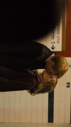 a man and woman standing next to each other in front of a subway station sign