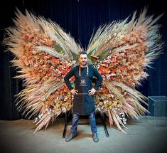 a man standing in front of a giant butterfly made out of fake flowers and feathers