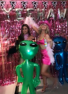 two women standing next to each other in front of pink and green tinsel balloons