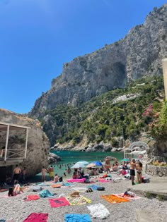 many people are on the beach with towels and umbrellas in front of some mountains