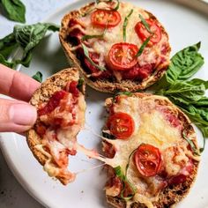 a person is taking a slice of pizza from a white plate with basil and tomatoes on it