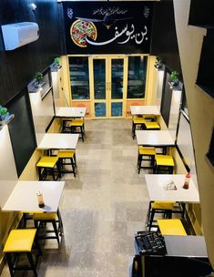 the interior of a restaurant with yellow tables and black walls, decorated in arabic script