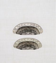 two metal handles with designs on them in front of a white wall and behind the door