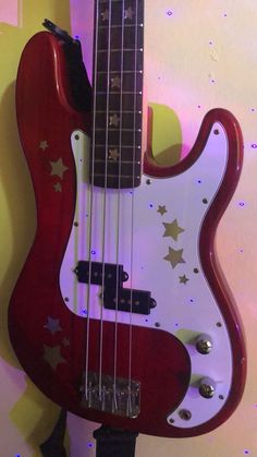 a red and white bass guitar with stars on it's body, hanging from the wall